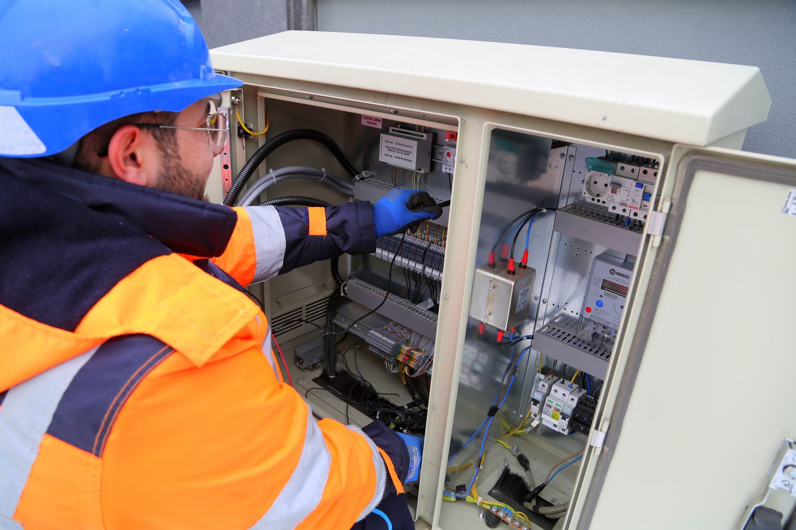 Profesional con casco y equipo de trabajo junto a un cuadro eléctrico